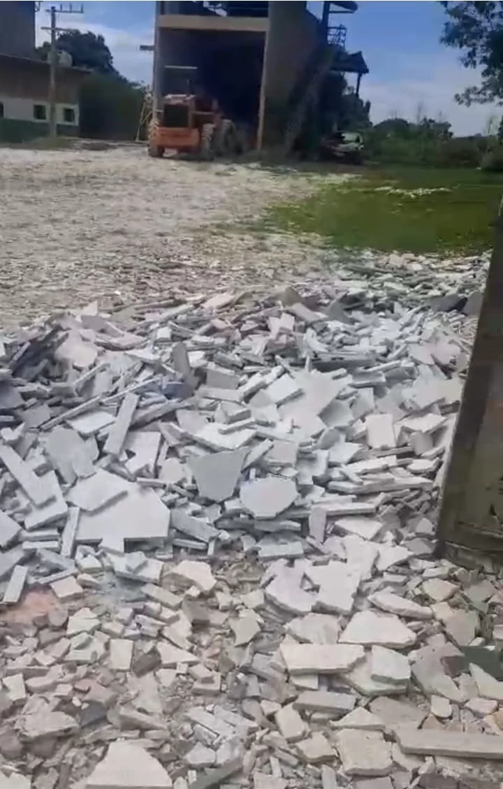 Resíduos de construção civil aguardando trituração — máquina e galpão ao fundo